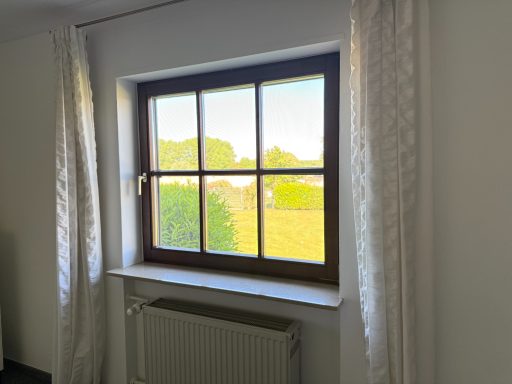 Fenster mit Holzrahmen, weißen Vorhängen und Blick auf den Garten.