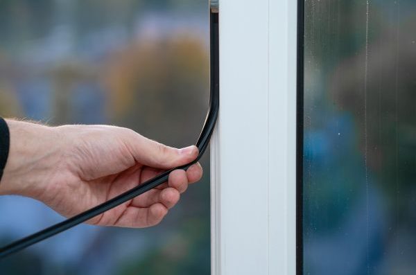 Eine Hand zieht eine Dichtung durch einen Fensterrahmen.
