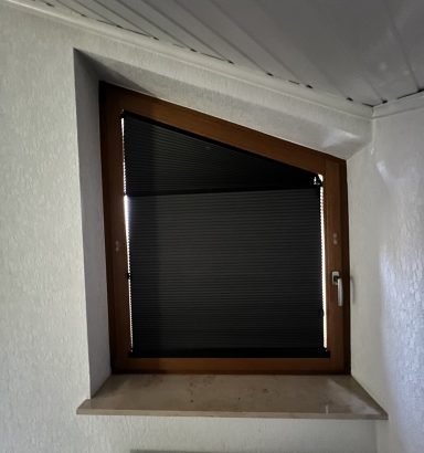 Dachfenster mit schwarzem Sichtschutz und braunem Holzrahmen in einem hellen Raum.