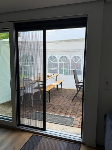 Türe mit Blick auf eine Terrasse und Gartenmöbel in einem geschützten Bereich.