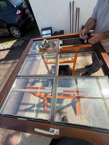 Ein Handwerker repariert ein Holzfenster auf einem Gestell im Freien.