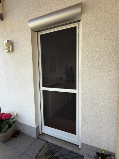 Weiße Fliegengittertür mit silbernem Oberteil und Umgebung aus grauen Fliesen.