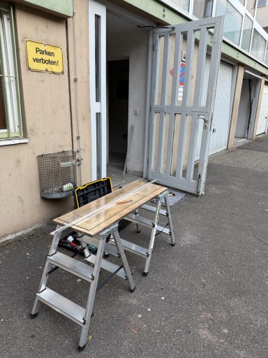 Eine Holzleiter steht vor einer geöffneten Tür in einem Gebäude.
