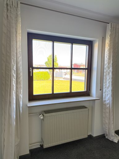 Holzfenster mit vier Rahmen, Vorhängen und Heizkörper, Blick auf einen grünen Außenbereich.