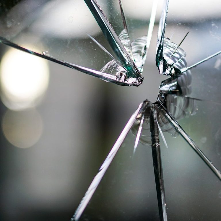 Nahaufnahme eines zerbrochenen Glases mit scharfen Bruchkanten und unscharfem Hintergrund.