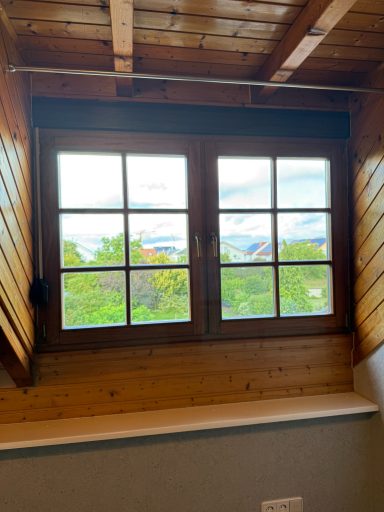 Holzfenster mit mehreren Feldern, Blick auf grüne Bäume und Landschaft im Hintergrund.