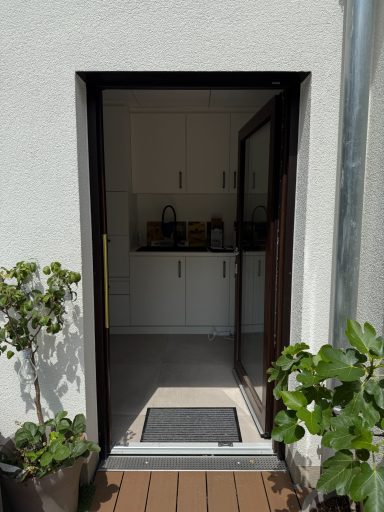 Blick auf eine offene Tür, die in eine helle Küche führt, umrahmt von Pflanzen.