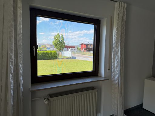 Blick aus einem Fenster auf eine grüne Wiese und einige Gebäude im Hintergrund.