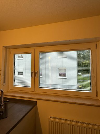 Blick aus einem Fenster auf ein graues Gebäude und den grünen Garten daneben.