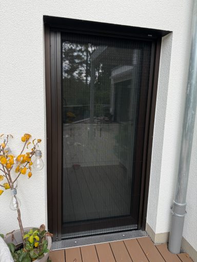 Schwarze Schiebetür mit Sicht auf den Garten und einem Topf mit gelben Blumen daneben.