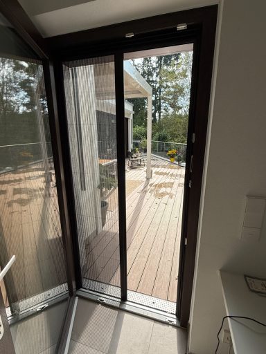 Glas-Schiebetür mit Blick auf eine Terrasse und Garten im Hintergrund.