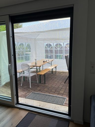 Blick auf eine Terrasse mit Tisch und Stühlen durch ein Glas-Schiebetür.