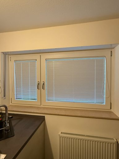 Fenster mit weißen Jalousien und grauer Fensterbank in einer hellen Umgebung.