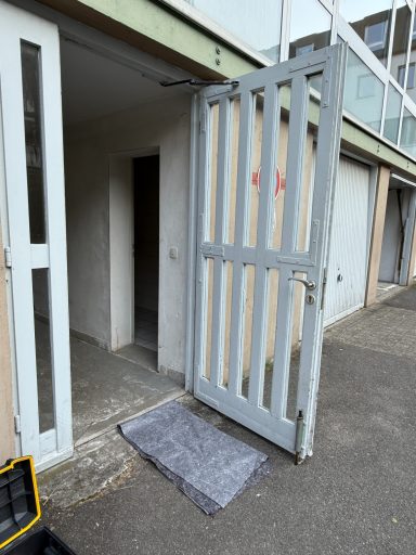 Offene Eingangstür mit einem grauen Teppich davor an einem modernen Gebäude.