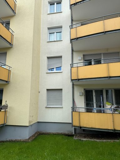Fassade eines Mehrfamilienhauses mit Balkonen und grünem Rasen im Vordergrund.
