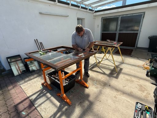 Ein Handwerker arbeitet an einem Tisch im Freien mit Werkzeugen und Materialien.